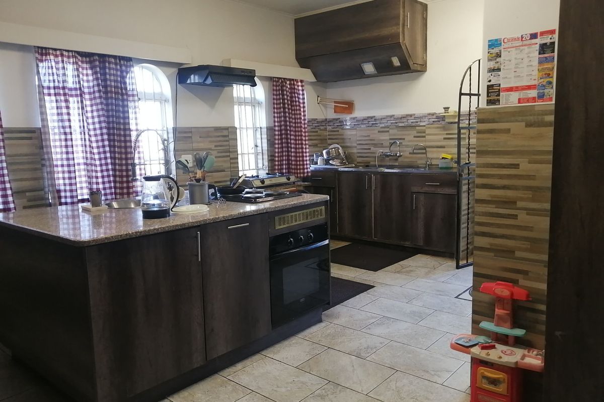 A functional kitchen featuring dark wood cabinetry, granite countertops, a built-in oven, hob, and tiled finishes throughout.