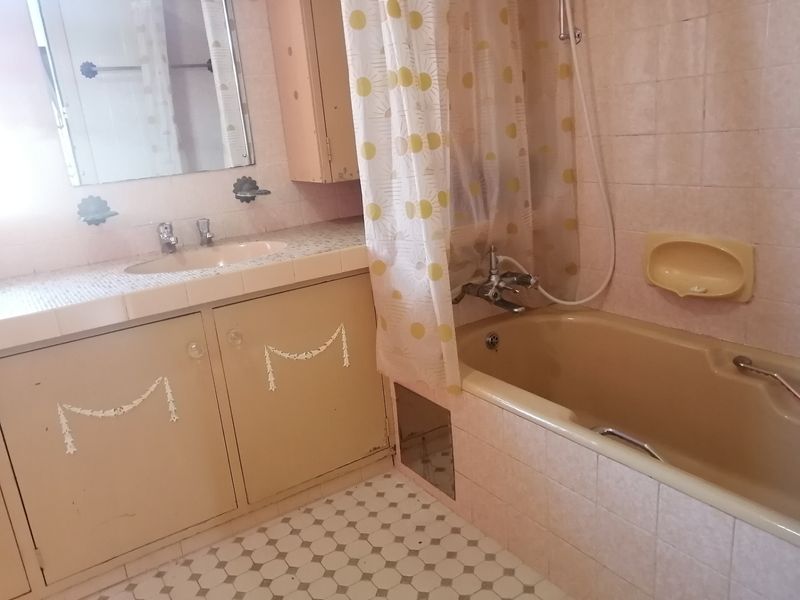 A dated bathroom featuring a built-in vanity with tiled countertop, integrated sink, and a bathtub with shower mixer, requiring modernization of finishes.