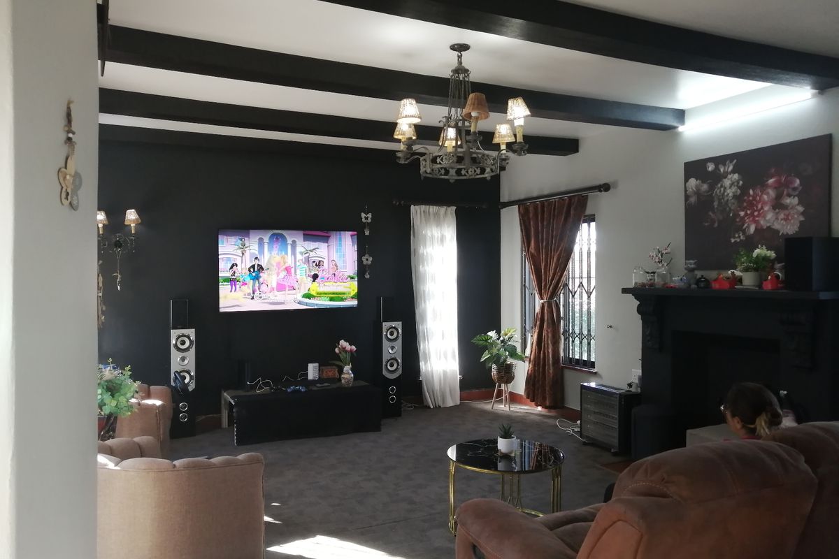 Spacious living room featuring exposed dark ceiling beams, a central fireplace, and a decorative chandelier, creating a cozy and traditional atmosphere.