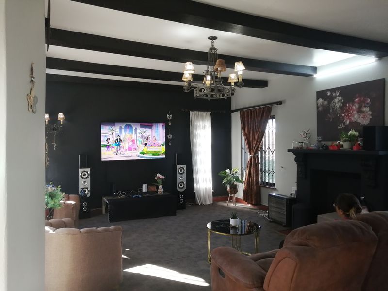 Spacious living room featuring exposed dark ceiling beams, a central fireplace, and a decorative chandelier, creating a cozy and traditional atmosphere.