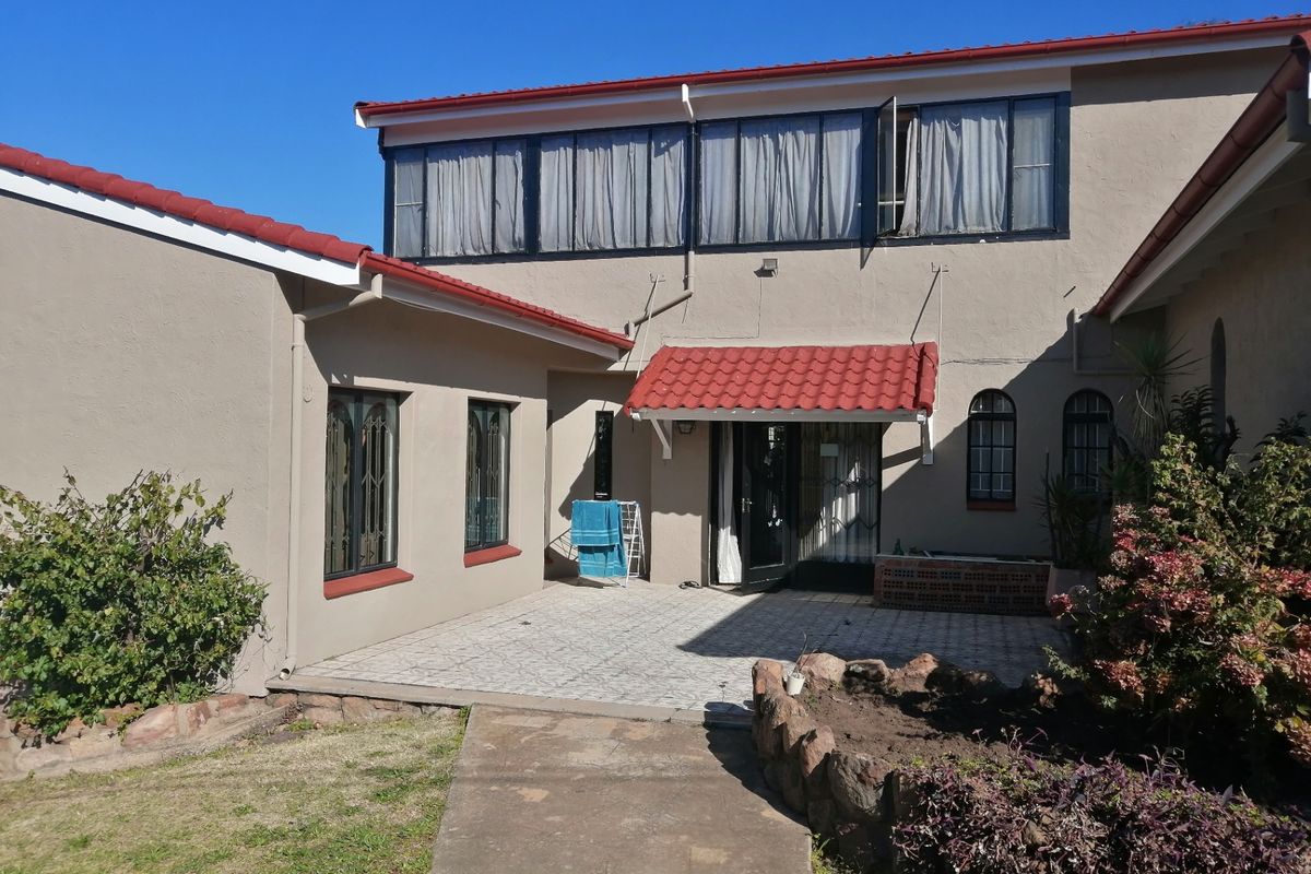 Rear exterior view of the house featuring a tiled patio area, stone garden borders, and a red tiled roof with security-fitted windows.