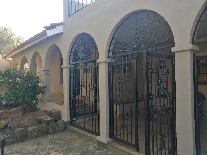 A covered patio area featuring arched masonry columns, decorative wrought iron security gates, and tiled flooring.