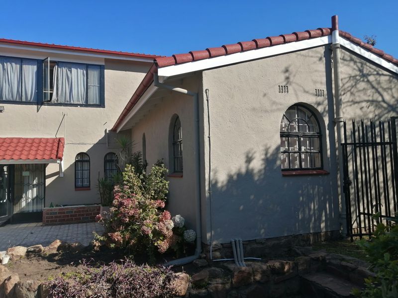 Rear view of the house featuring plastered walls, terracotta roof tiles, arched windows, and a paved patio area.