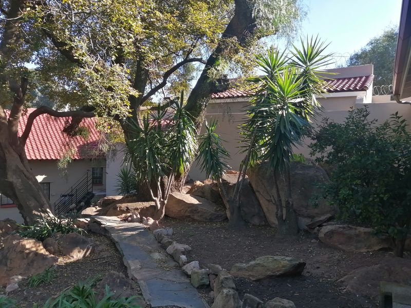 A landscaped garden area featuring a stone pathway, natural rockery, and mature trees, set against the backdrop of the property's exterior.