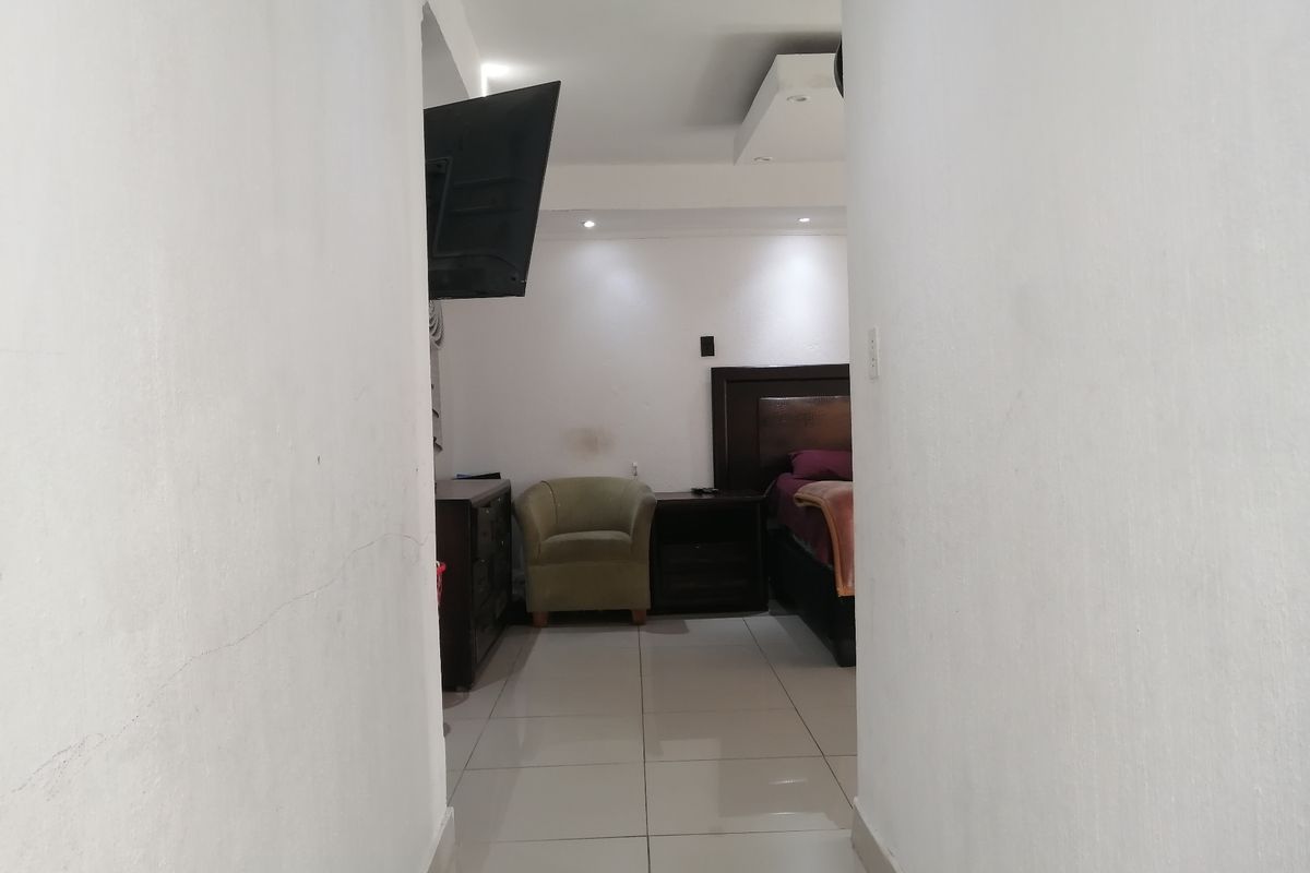 A view into a bedroom featuring tiled flooring and recessed ceiling lighting, accessed through a narrow hallway.