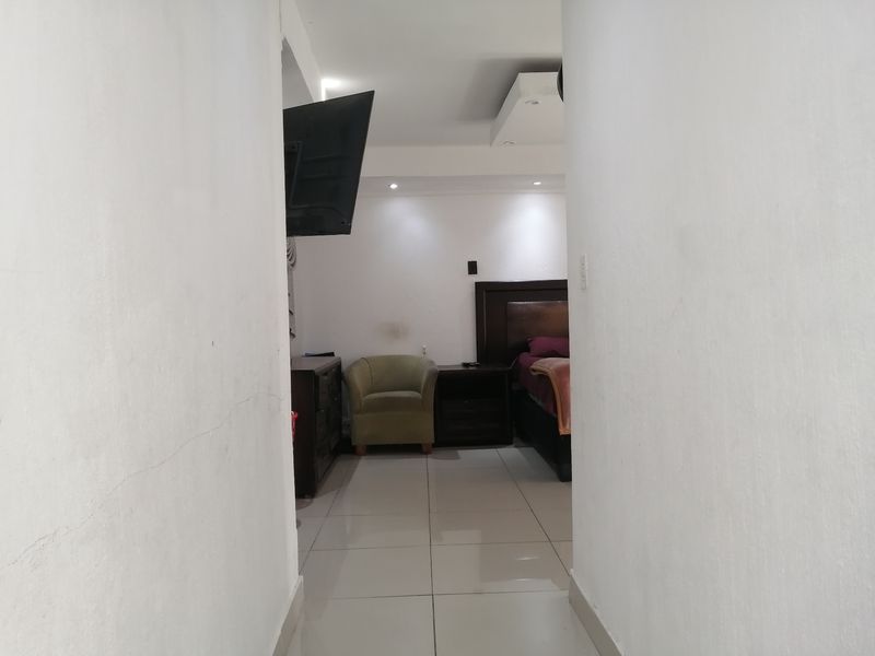 A view into a bedroom featuring tiled flooring and recessed ceiling lighting, accessed through a narrow hallway.