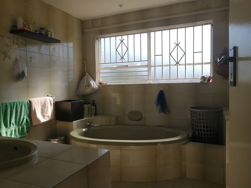 A dated bathroom featuring a built-in bathtub, tiled vanity, and security bars on the window, offering potential for modernization.