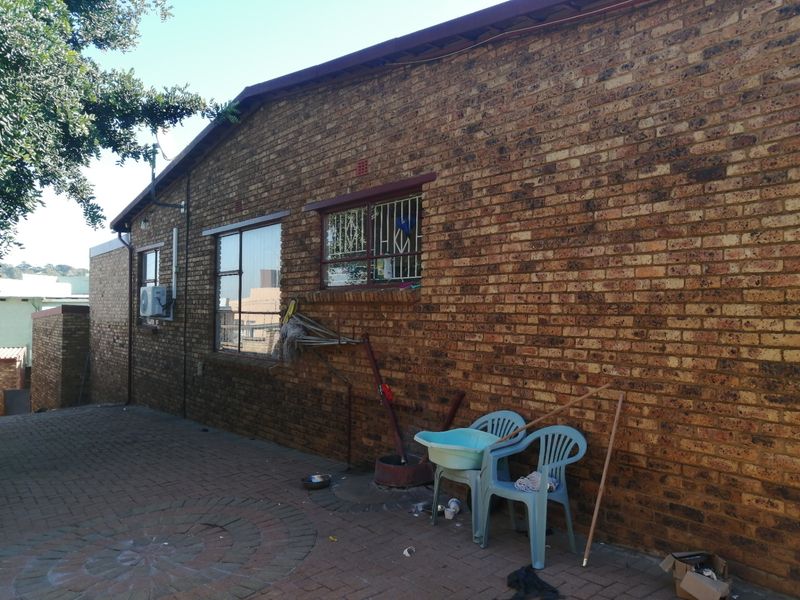 Rear exterior view of the house featuring a face brick facade, paved patio area, and security bars on the windows.