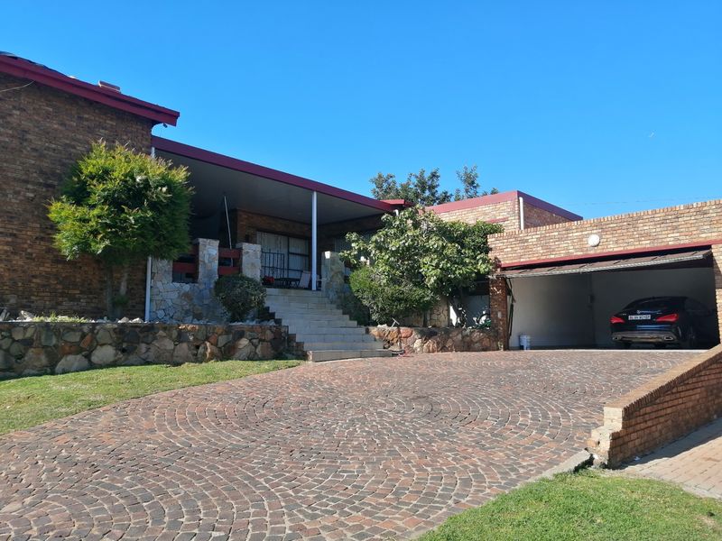 Front elevation of a brick house featuring a cobblestone driveway, double garage, and a raised covered patio area with stone masonry accents.