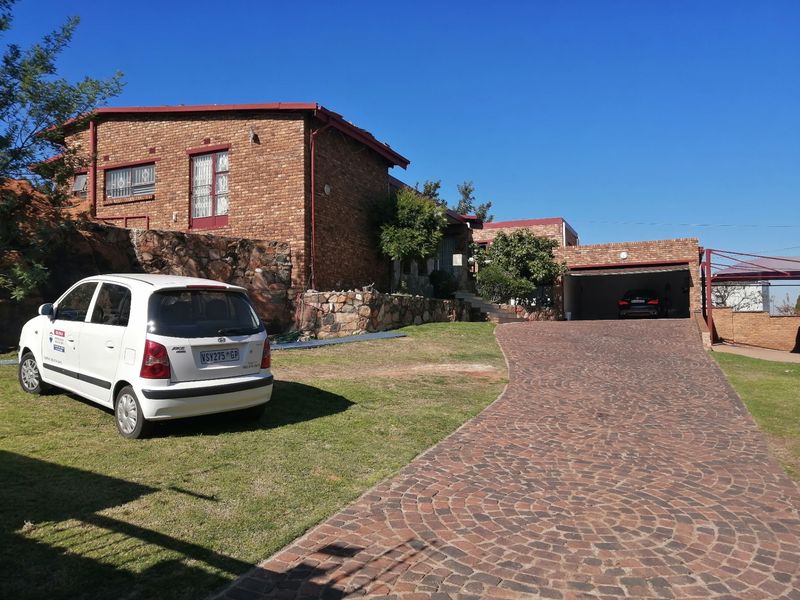 Front exterior view of a face brick house featuring a large cobblestone driveway, stone retaining wall, and an integrated double garage.