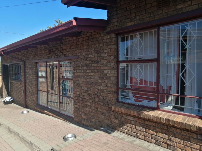 Rear exterior view of the house featuring a face brick facade, paved patio area, and windows fitted with security bars.