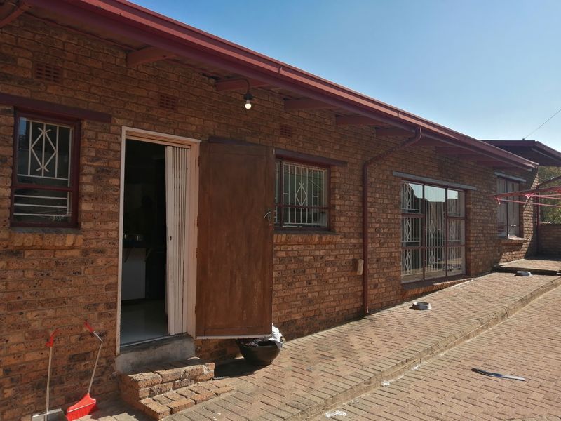 Rear exterior view of a face brick house featuring a paved patio area, metal security gates, and a corrugated metal roof.