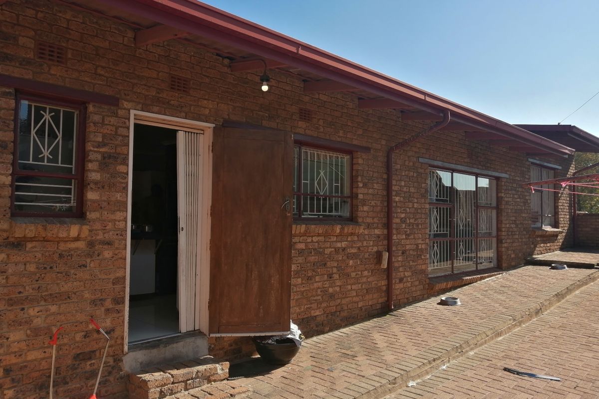 Rear exterior view of a face brick house featuring a paved patio area, metal security gates, and a corrugated metal roof.