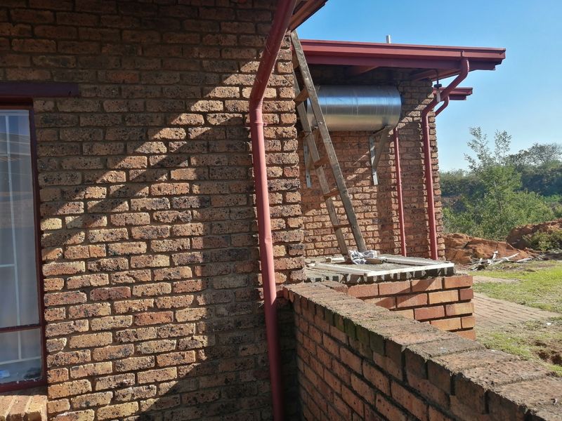 Rear exterior view of the property featuring face brick walls, a solar water heater geyser, and a brick boundary wall.