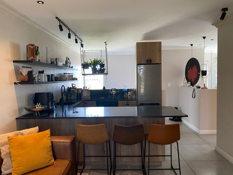 Modern open-plan kitchen featuring dark stone countertops, wood-finish cabinetry, integrated appliances, and a breakfast bar, seamlessly flowing into the living area.