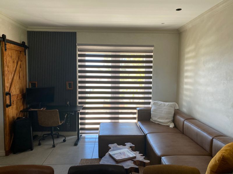 A modern home office featuring a sliding barn door, decorative slatted wall paneling, tiled flooring, and large windows with roller blinds.