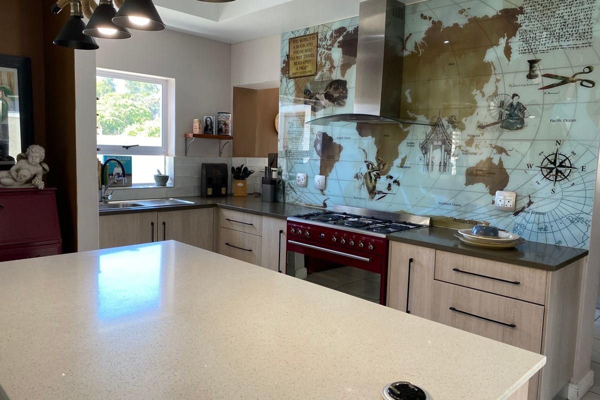 Modern kitchen featuring a large island with quartz countertops, gas range, stainless steel extractor fan, and a unique decorative world map glass splashback.
