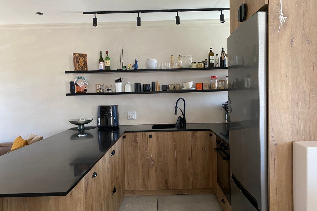 Modern kitchen featuring wood-grain cabinetry, black stone countertops, floating shelves, and integrated appliances with contemporary track lighting.