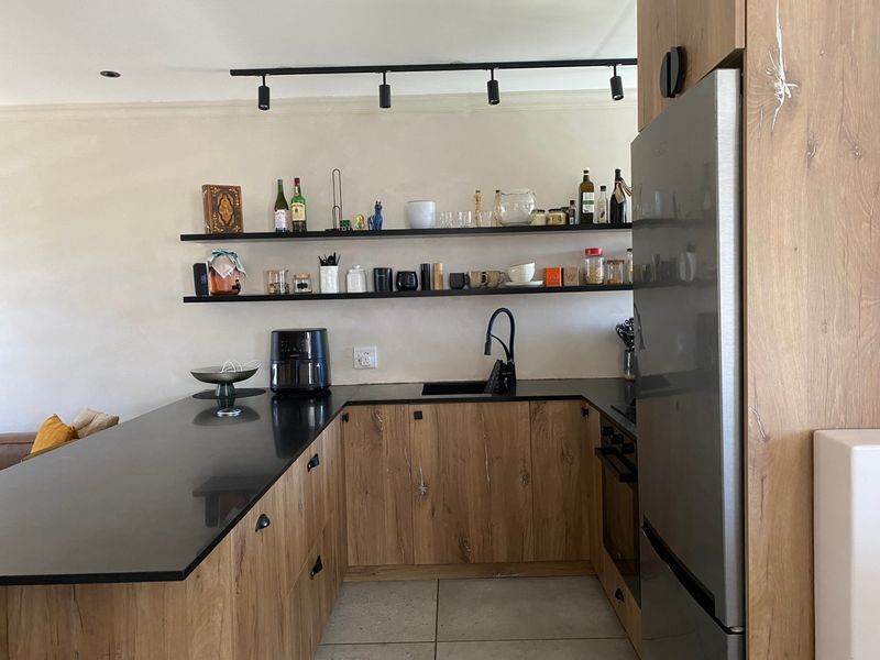 Modern kitchen featuring wood-grain cabinetry, black stone countertops, floating shelves, and integrated appliances with contemporary track lighting.