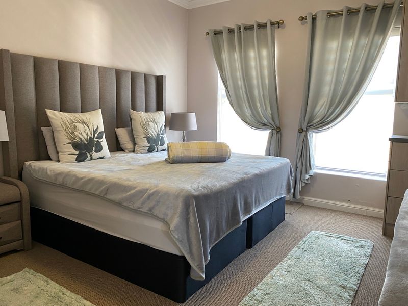 A well-maintained bedroom featuring neutral wall tones, carpeted flooring, and dual windows with installed curtain rods.