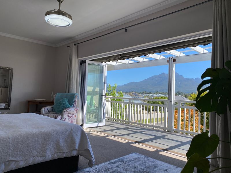 Spacious bedroom featuring large bi-fold doors opening onto a balcony with a pergola and scenic mountain views.