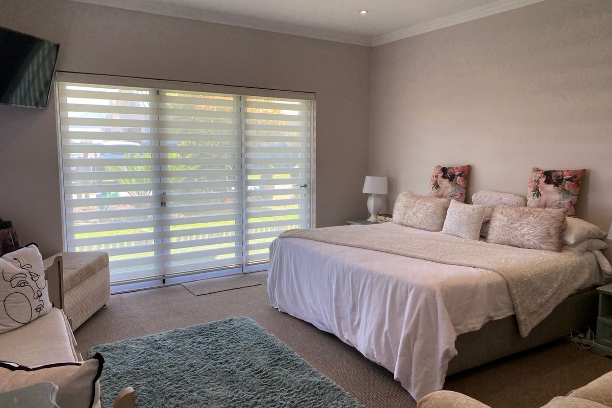 Spacious bedroom featuring large sliding glass doors with modern blinds, recessed ceiling lighting, and neutral carpeting.
