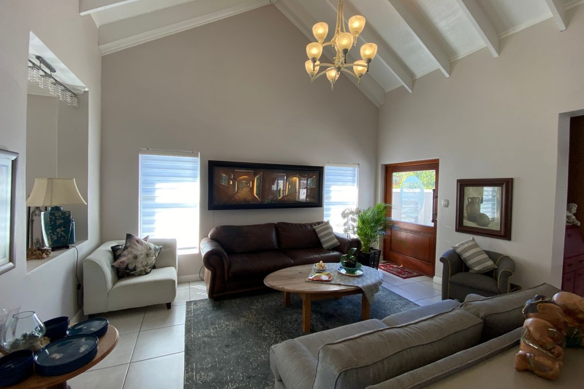 Spacious living room featuring a high vaulted ceiling with exposed rafters, tiled flooring, and a timber entrance door, creating a bright and airy atmosphere.