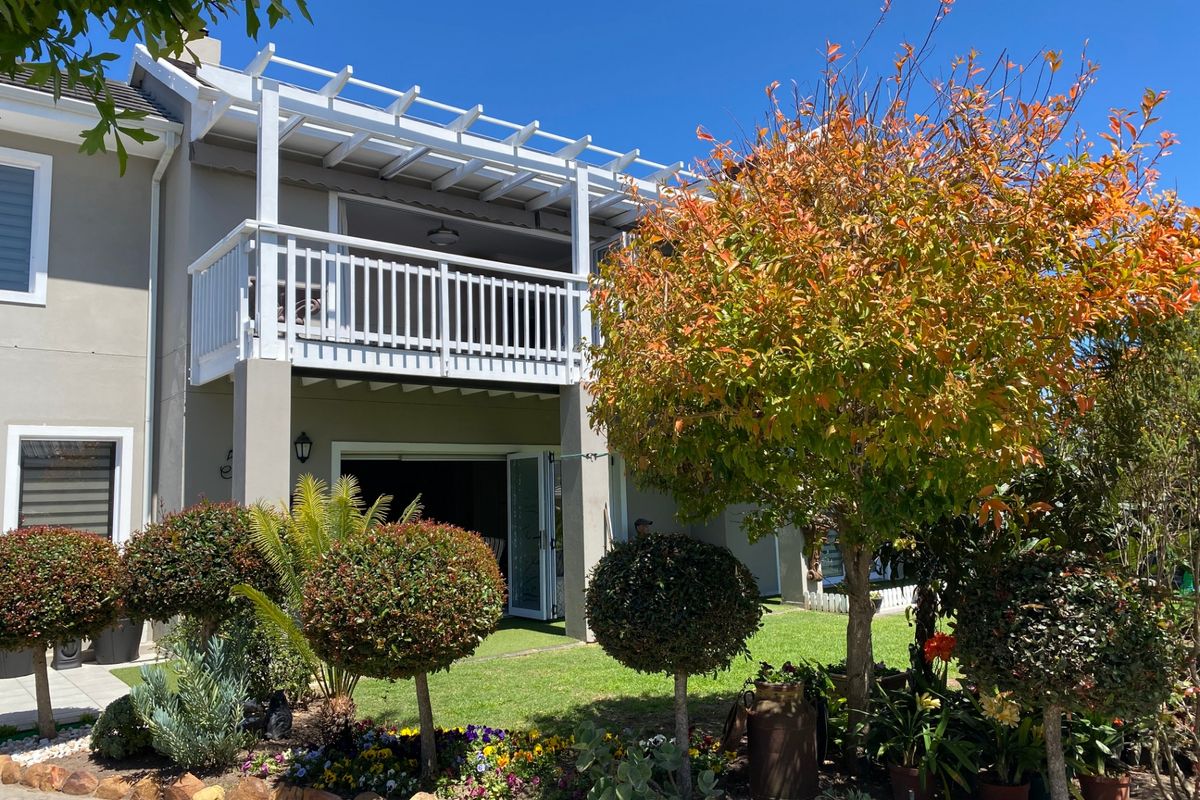 Rear view of the property featuring a landscaped garden, a ground-level patio area with bi-fold doors, and an upper-level balcony with a white pergola.
