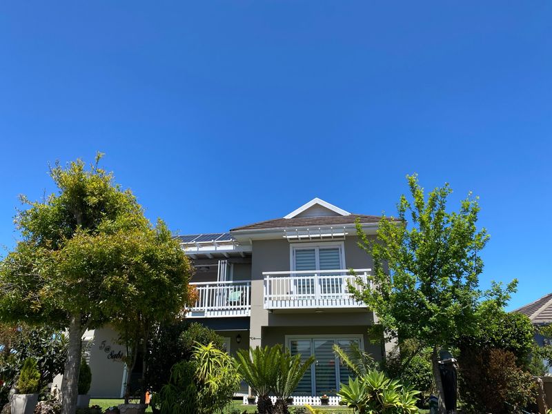 Front elevation of a two-story residential house featuring a balcony, tiled roof, and installed solar panels, surrounded by established garden landscaping.