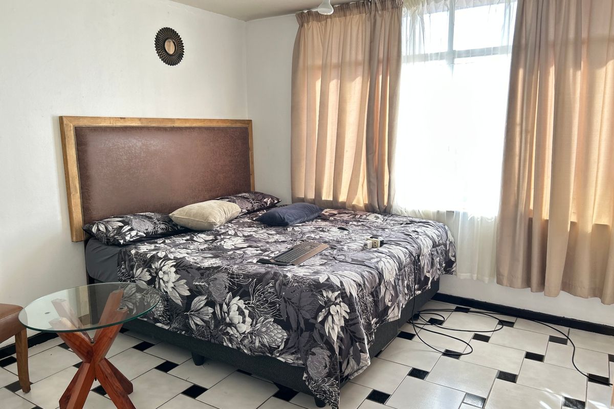 A bedroom featuring large windows with curtains, a ceiling fan, and tiled flooring with a decorative pattern.