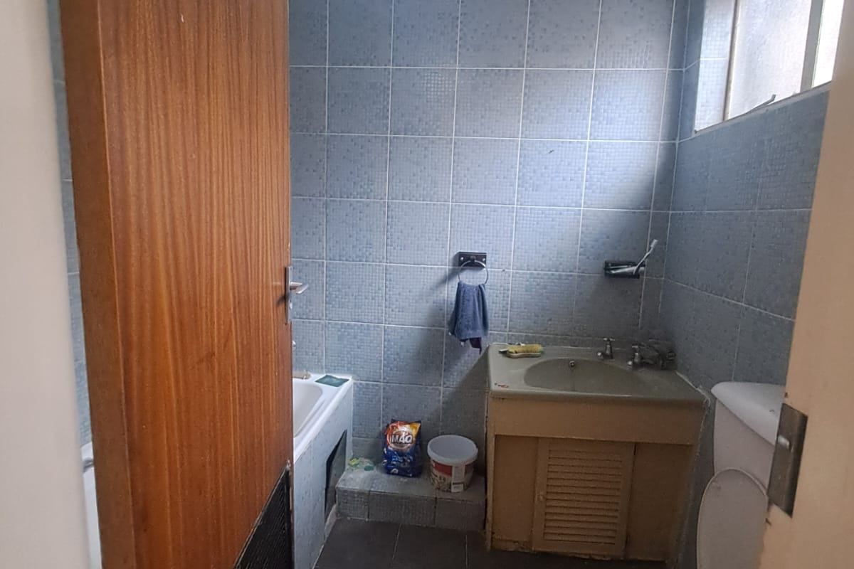 A compact bathroom featuring dated blue wall tiles, a vanity sink, a toilet, and a bathtub, requiring modernization.