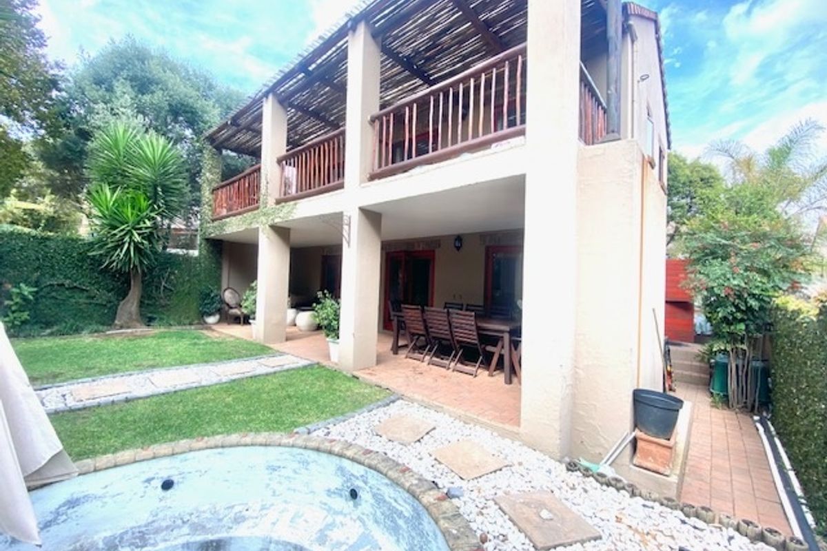 Rear view of a two-story house featuring a covered ground-floor patio, an upper-level balcony with timber railings, and an outdoor swimming pool.