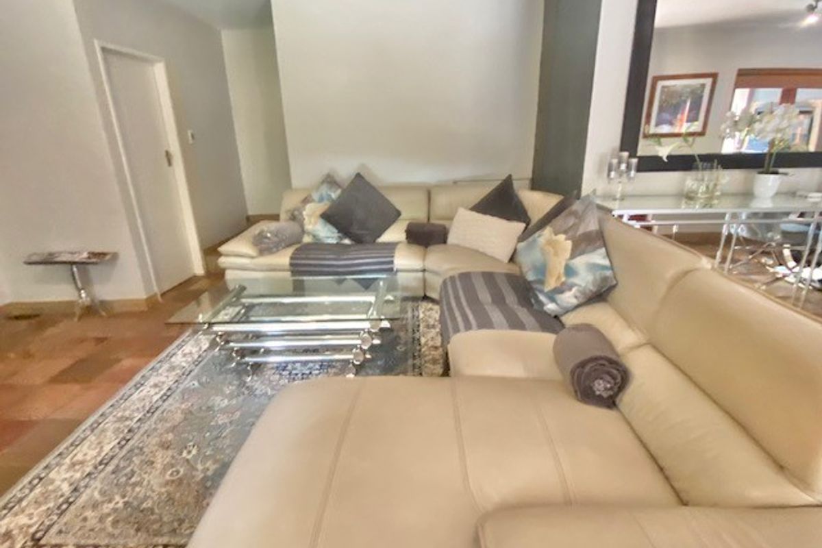 A spacious living room featuring tiled flooring and a large wall-mounted mirror, providing a neutral base for interior design updates.