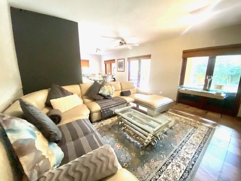 Spacious living room featuring tiled flooring, a ceiling fan, and large sliding glass doors providing natural light and garden access.