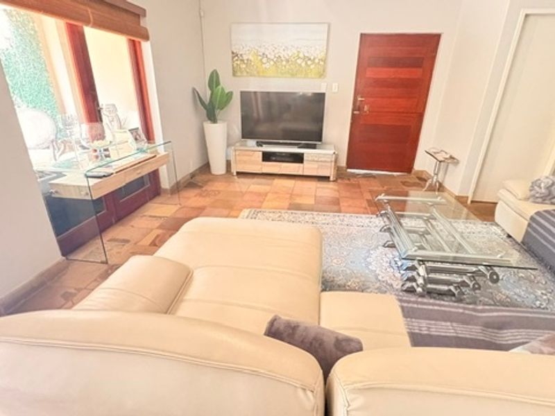 A living room featuring terracotta floor tiles, a wooden entrance door, and a sliding glass door providing access to the patio area.