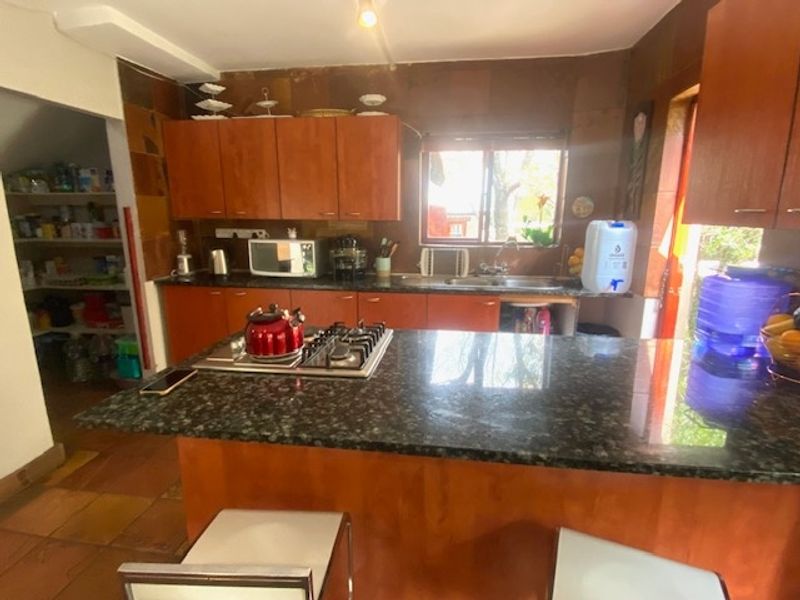 A functional kitchen featuring granite countertops, a built-in gas hob, wooden cabinetry, and an adjacent walk-in pantry area.