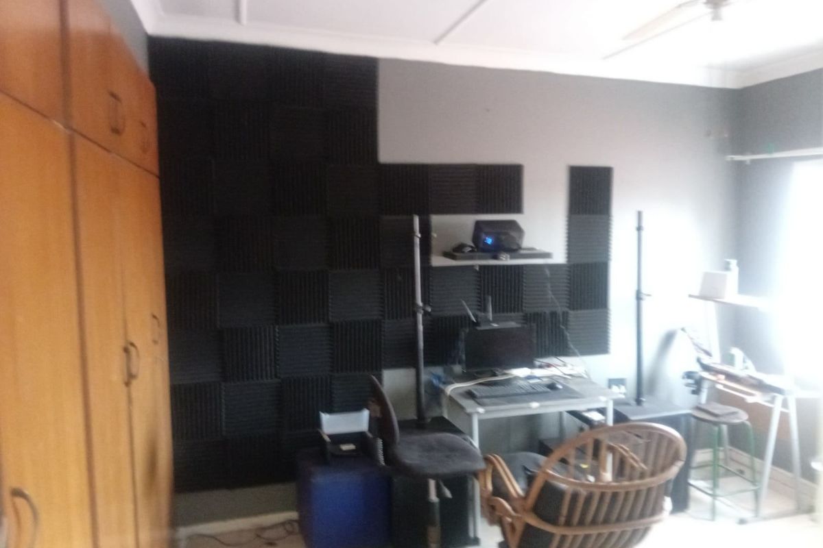 A bedroom featuring built-in wooden cupboards, a ceiling fan, and acoustic wall paneling, currently utilized as a home office or studio space.