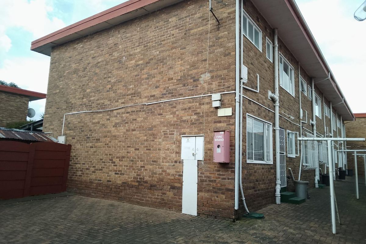 Rear exterior view of a multi-story apartment building featuring face brick construction, paved ground area, and installed fire safety equipment.