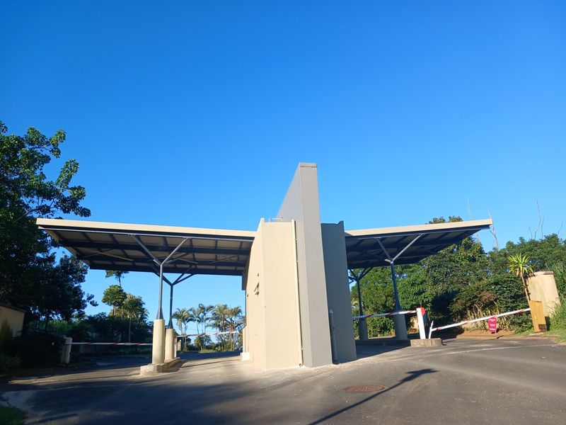 A modern security gatehouse entrance featuring a dual boom gate system and a covered driveway structure, providing controlled access to the residential estate.
