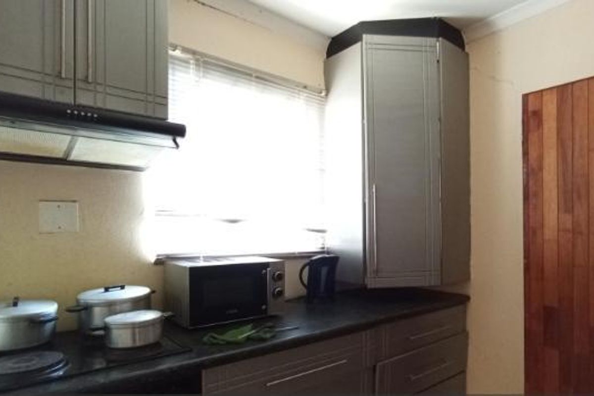 A compact kitchen featuring grey built-in cabinetry, an integrated extractor fan, a hob, and distinctive wooden wall paneling.