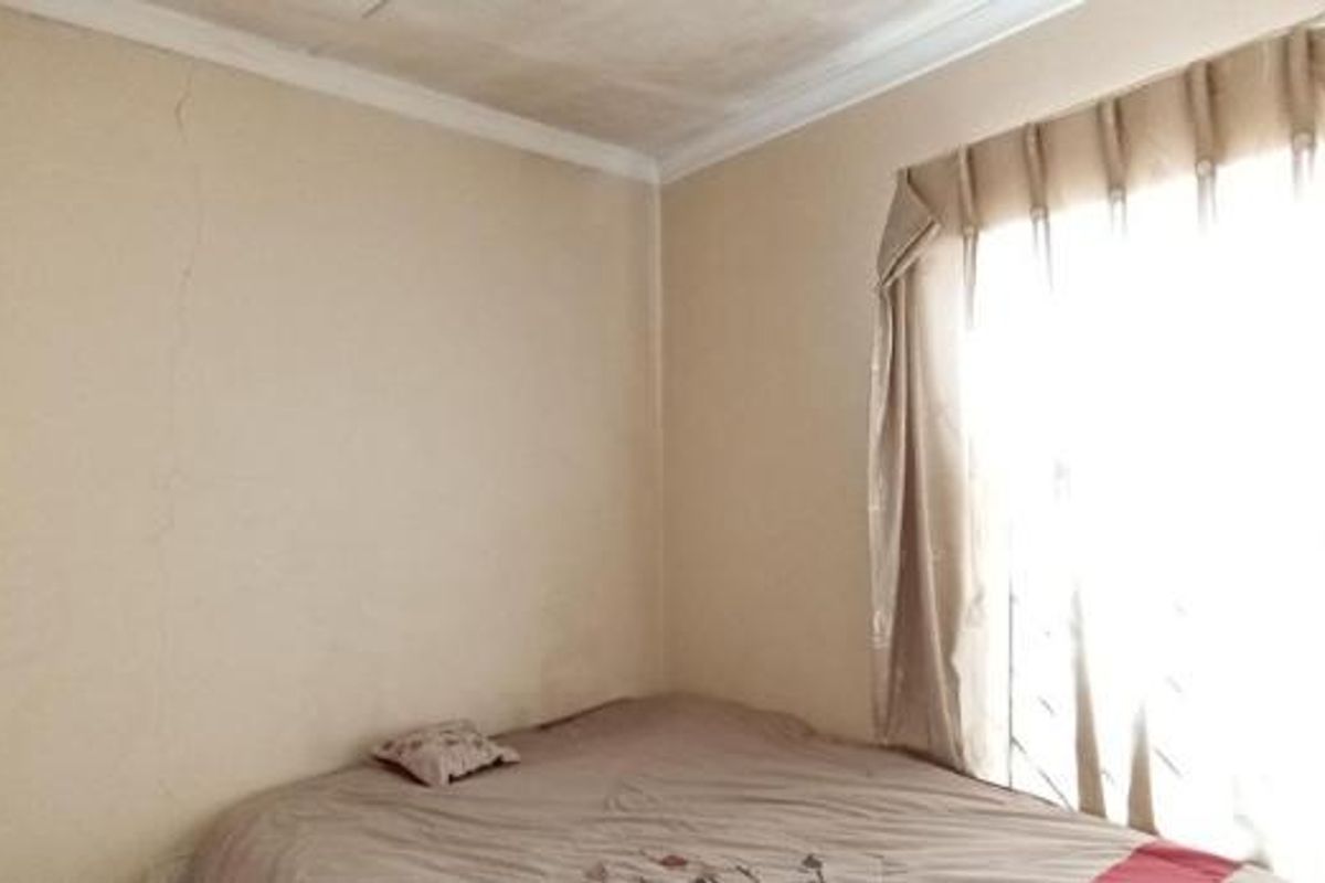 A bedroom featuring a built-in wardrobe and window security bars, showing signs of wall cracking requiring maintenance.