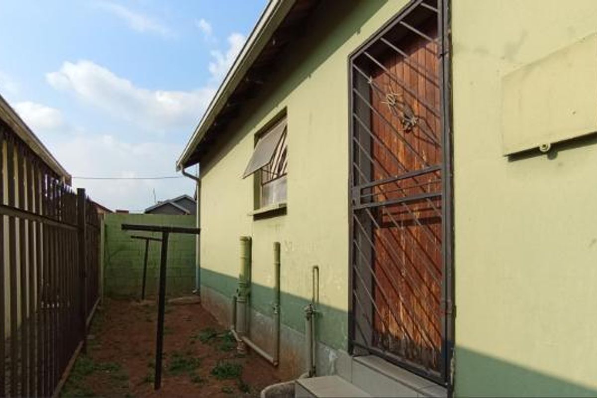 Side exterior view of the property featuring a security gate, metal fencing, and exposed exterior plumbing along the wall.