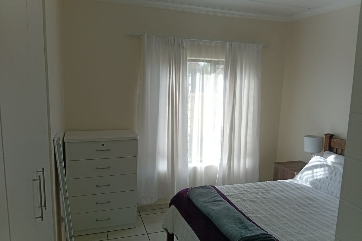 A functional bedroom featuring tiled flooring, a built-in wardrobe, and natural light through a window with curtains.