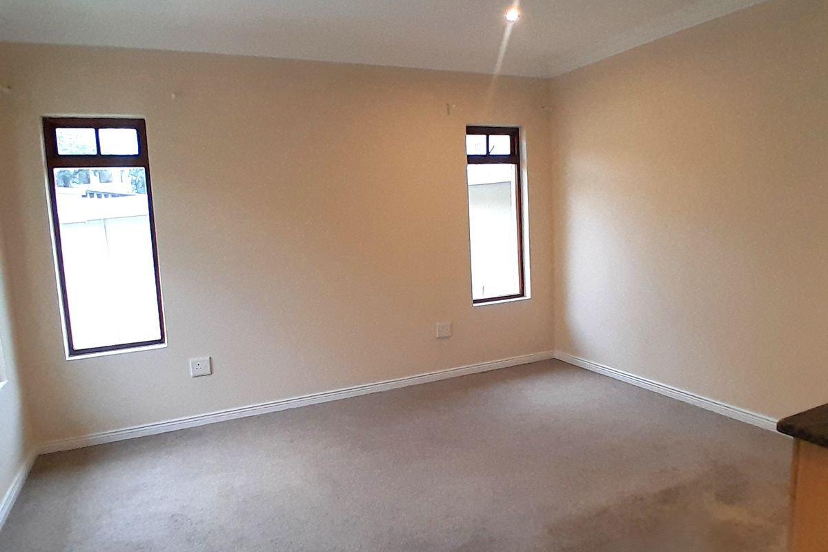 A spacious, empty bedroom featuring neutral wall tones, fitted carpeting, and two windows with dark frames, providing a blank canvas for personalization.