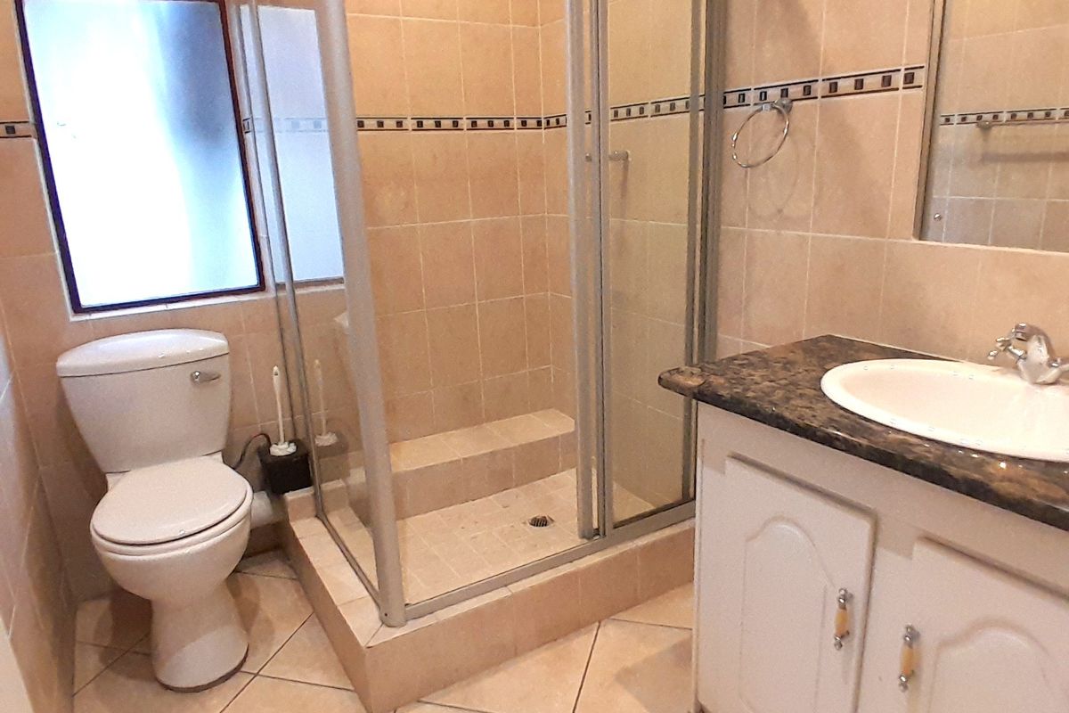 A functional bathroom featuring a glass-enclosed shower, a vanity with a stone-look countertop, and a standard toilet.