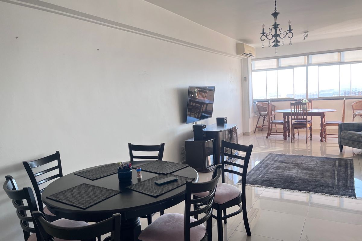 Spacious open-plan living and dining area featuring tiled flooring, a wall-mounted air conditioning unit, and large windows providing ample natural light.