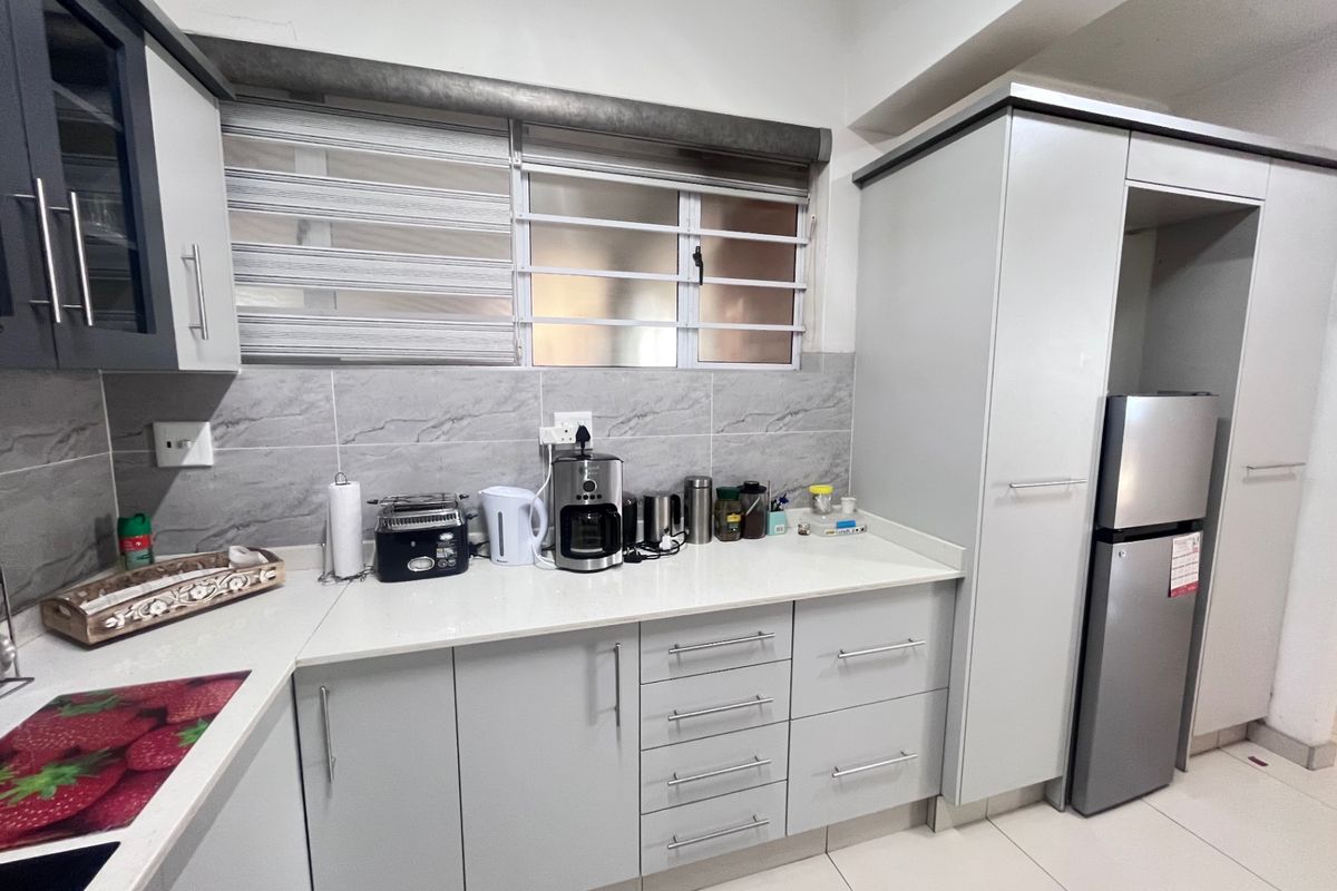 Modern kitchen featuring light grey cabinetry, stone countertops, tiled backsplash, and neutral floor tiles, offering a clean and functional workspace.