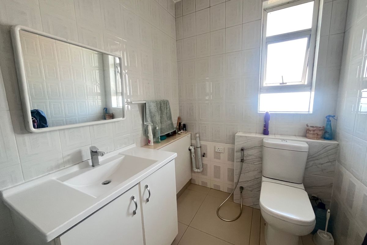 A functional bathroom featuring a vanity cabinet with basin, wall-mounted mirror, toilet with bidet spray, and tiled finishes throughout.