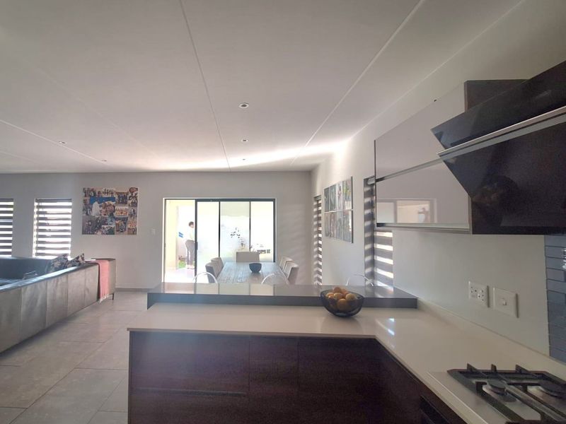 Modern open-plan living area featuring a sleek kitchen with stone countertops, gas hob, and seamless flow to the outdoor patio through sliding glass doors.