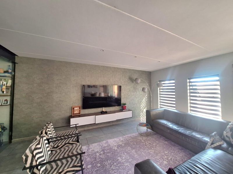 A modern living room featuring a textured feature wall, floating media console, tiled flooring, and recessed downlights with natural light from dual windows.
